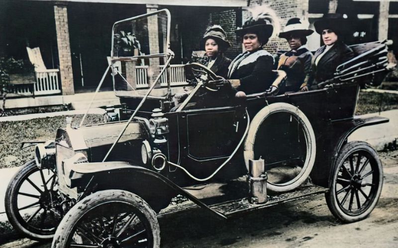 Photographie colorisée de Madame C. J. Walker, assise sur le siège du conducteur de sa première automobile, accompagnée de trois amies, 1911- maroons.black